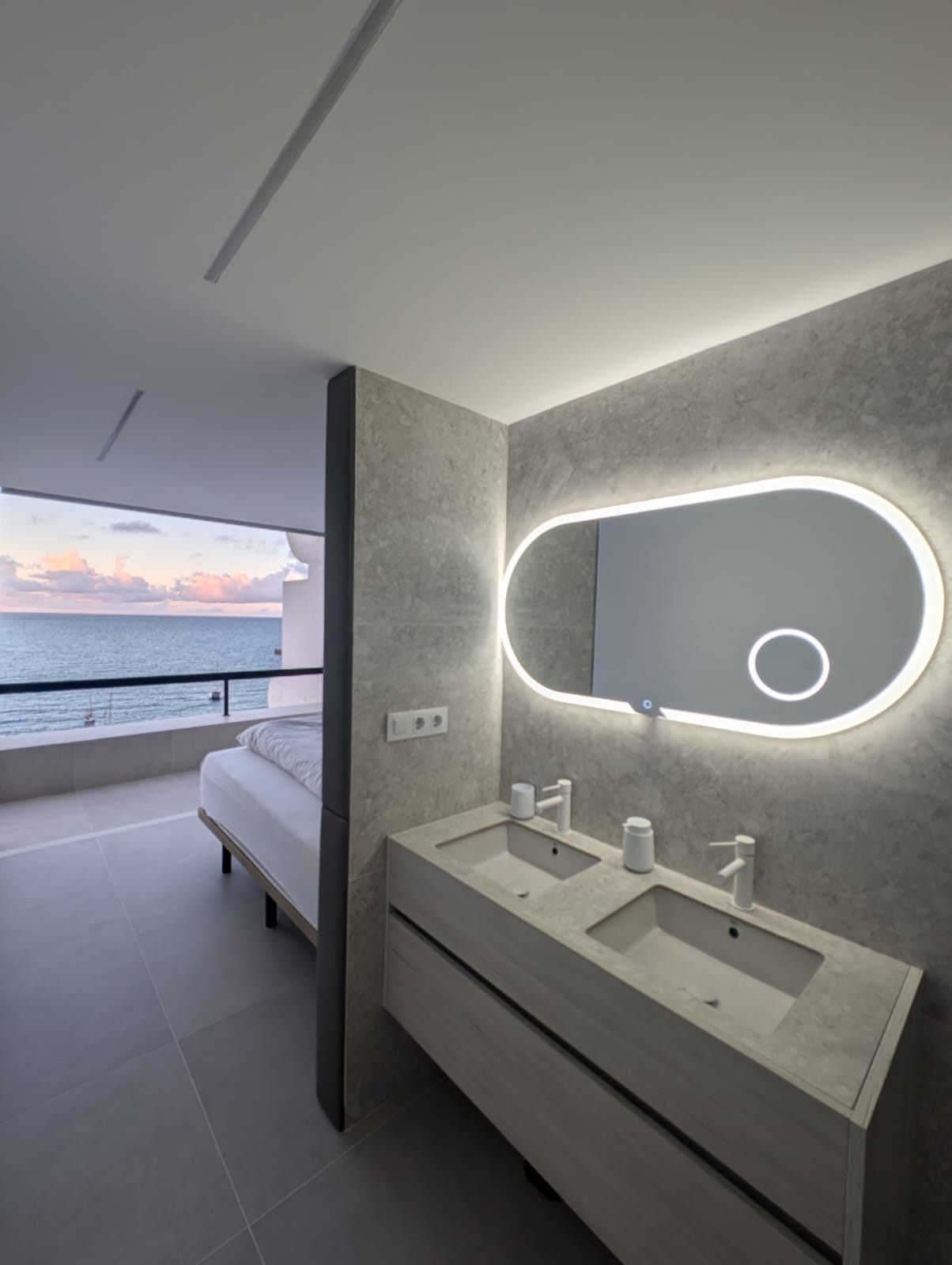 Offenes Bad mit Doppelwaschbecken, dahinter das Bett und das Meer