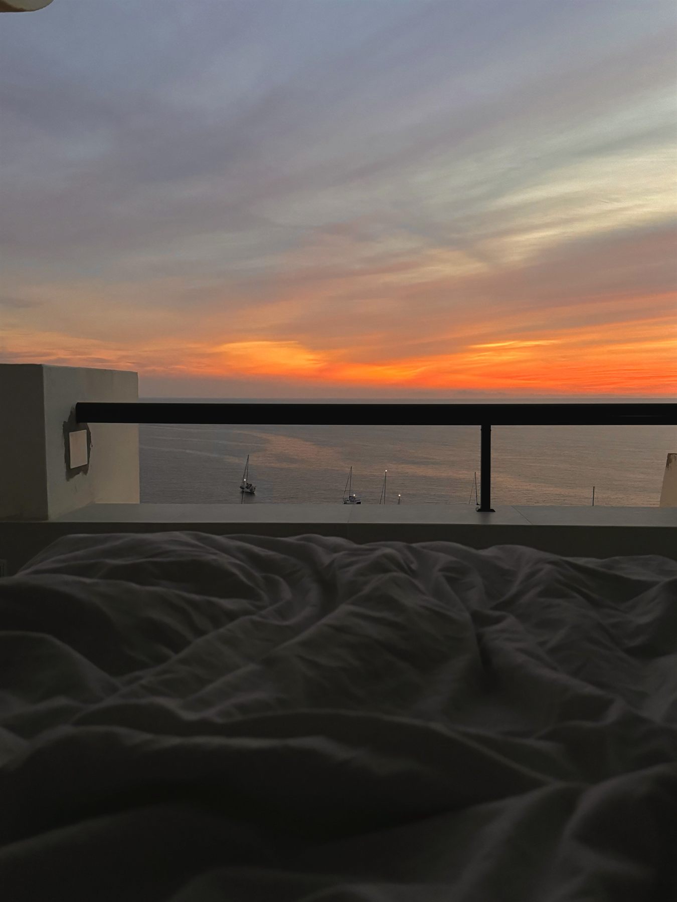 Sonnenuntergang über dem Meer, gesehen vom Bett aus über die Balkonbrüstung